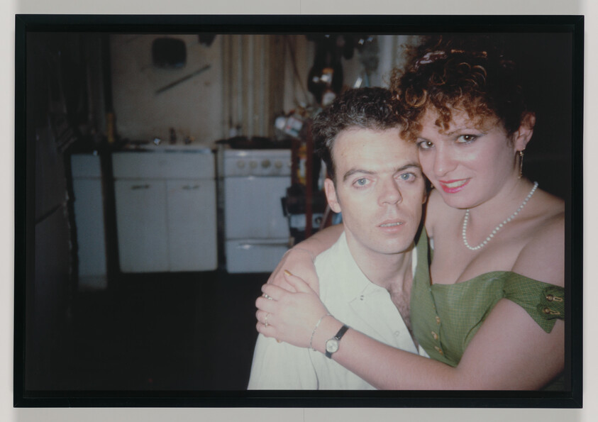 A woman embraces a man while they pose together in a dim kitchen.