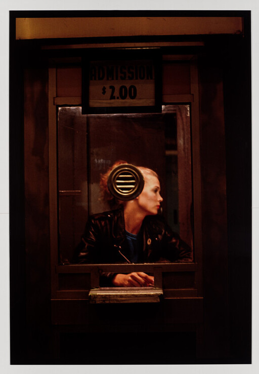 Woman in a dim ticket booth looks to the side beneath an "Admission $2.00" sign.