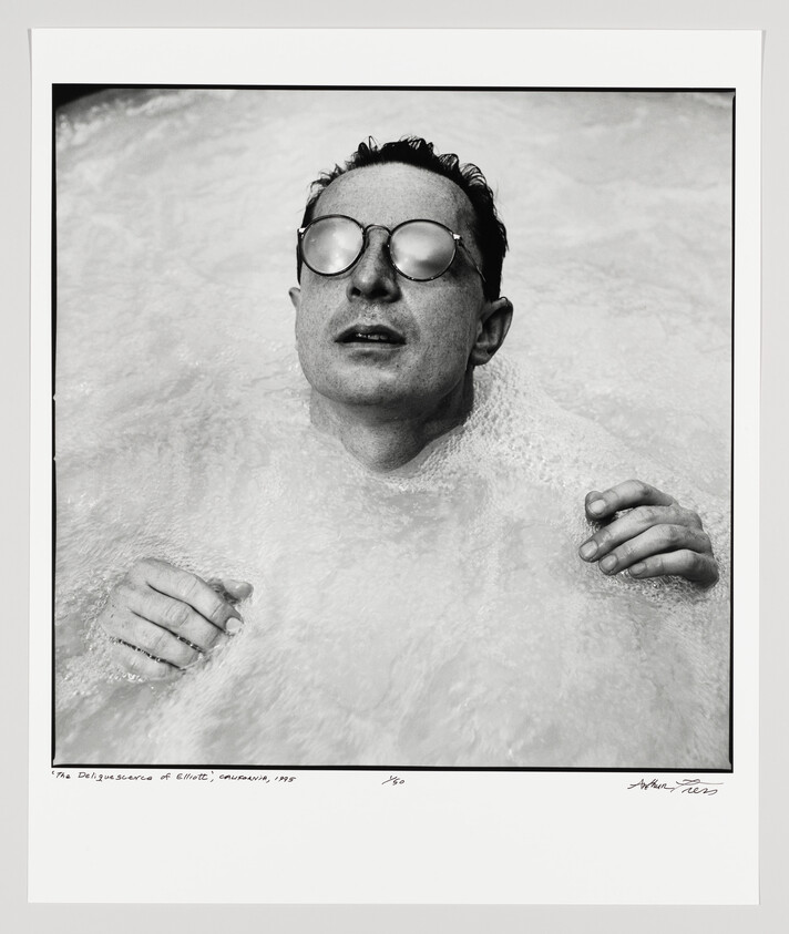 Person wearing round glasses floats in foamy water with eyes closed and hands visible.