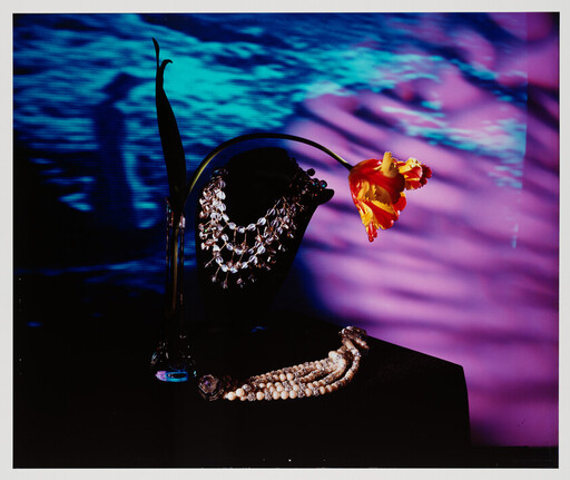 A black necklace stand with sparkling necklaces and a drooping orange tulip against a purple-blue backdrop.