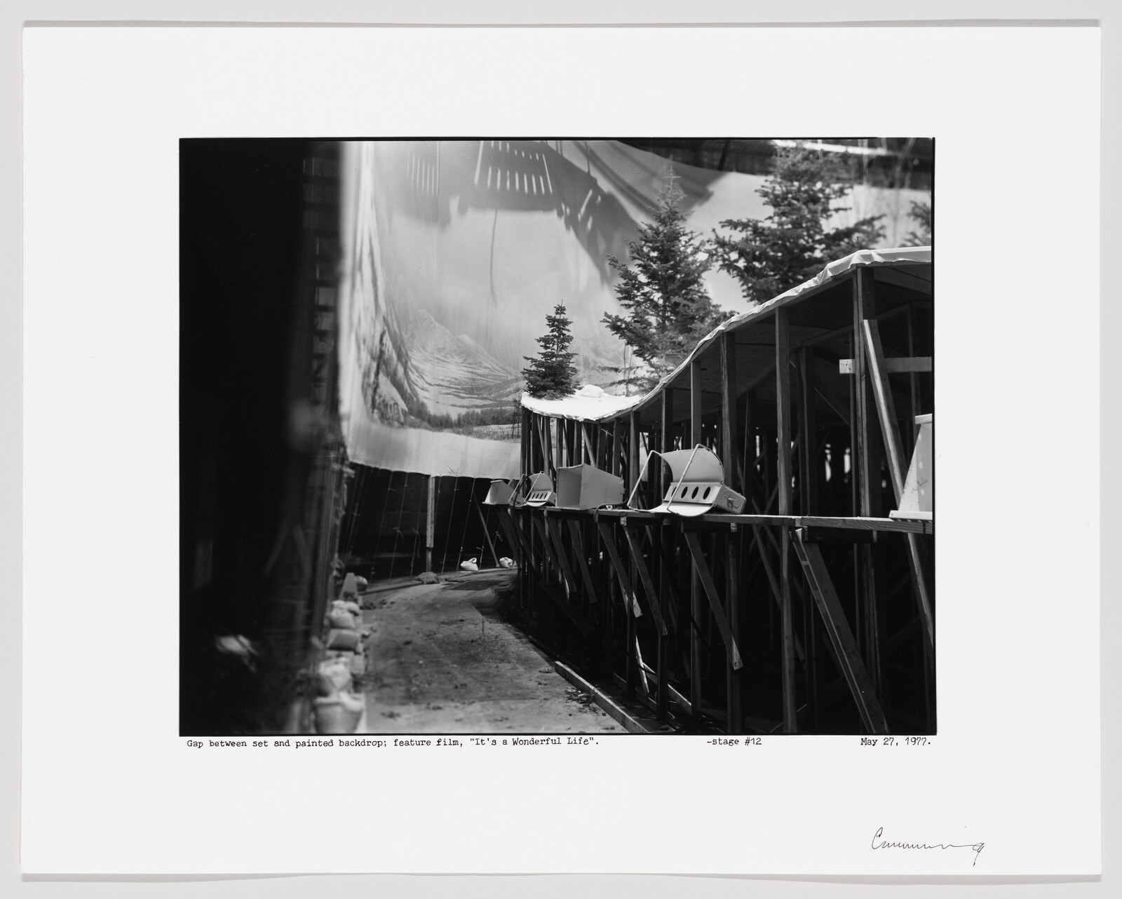 Backstage view showing gap between wooden set scaffolding and a painted snowy backdrop with props.