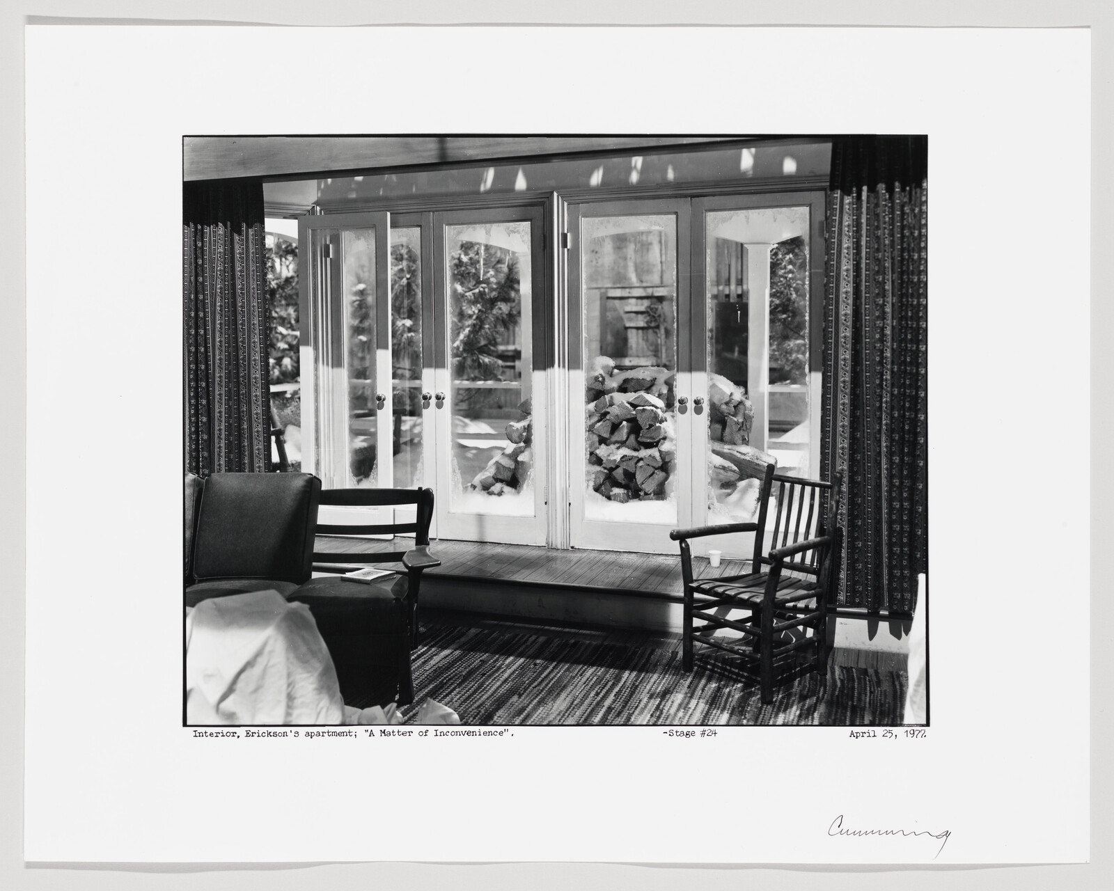 Living room with chairs facing glass doors showing stacked firewood and snow outside.