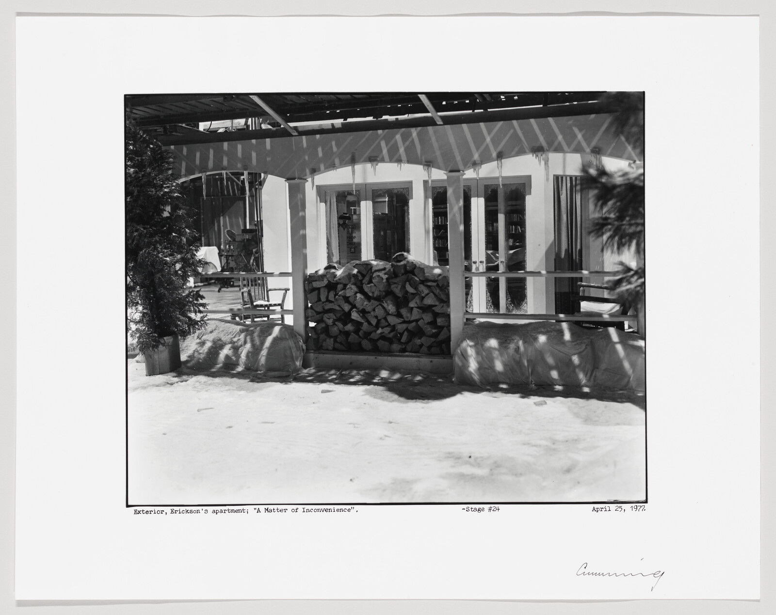A stacked pile of firewood sits on a snowy porch beneath hanging icicles.