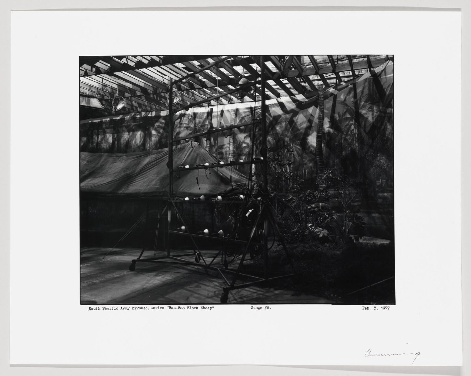 A stage set shows a canvas army bivouac tent and metal scaffolding under a glass roof.
