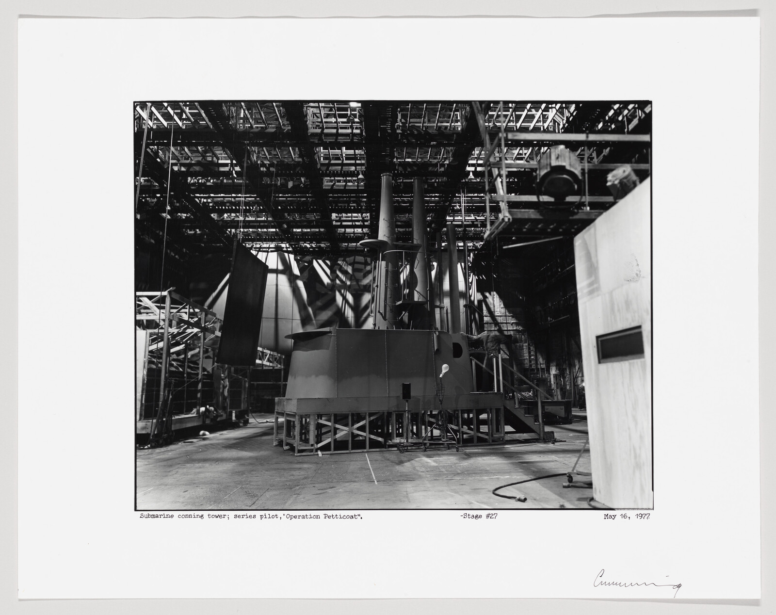 A submarine conning tower sits on a soundstage surrounded by scaffolding and lighting rigs.