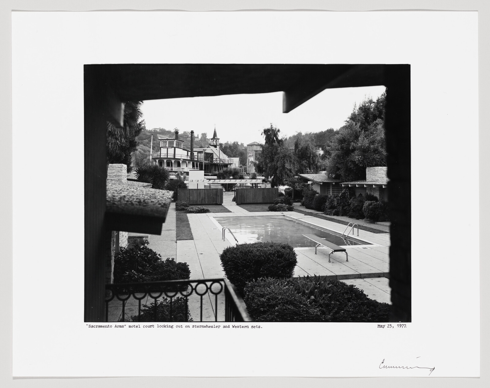 A motel courtyard with a swimming pool and surrounding rooms framed by a balcony railing.