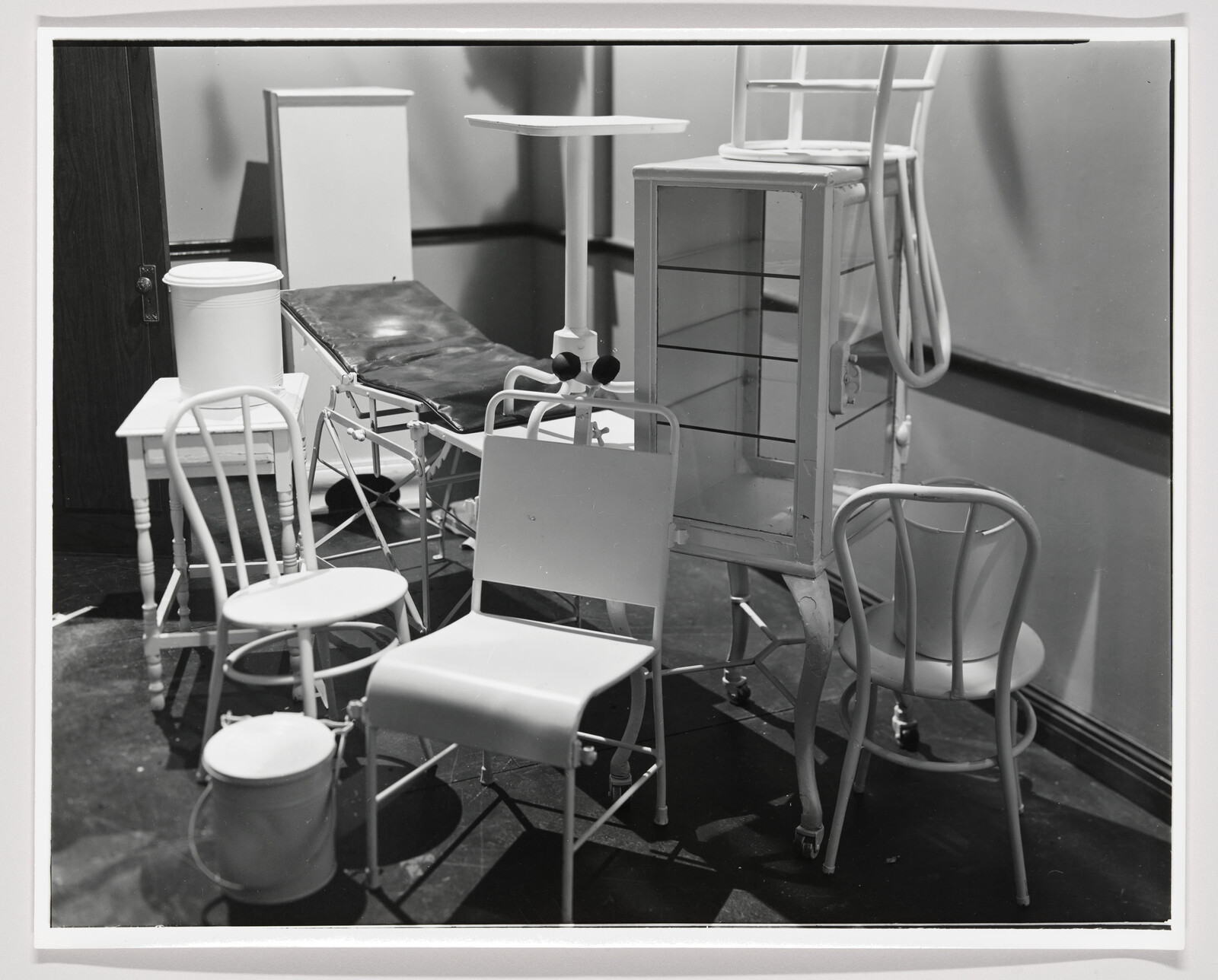 Various chairs, stools, and medical furniture crowded together around an exam table and cabinet.