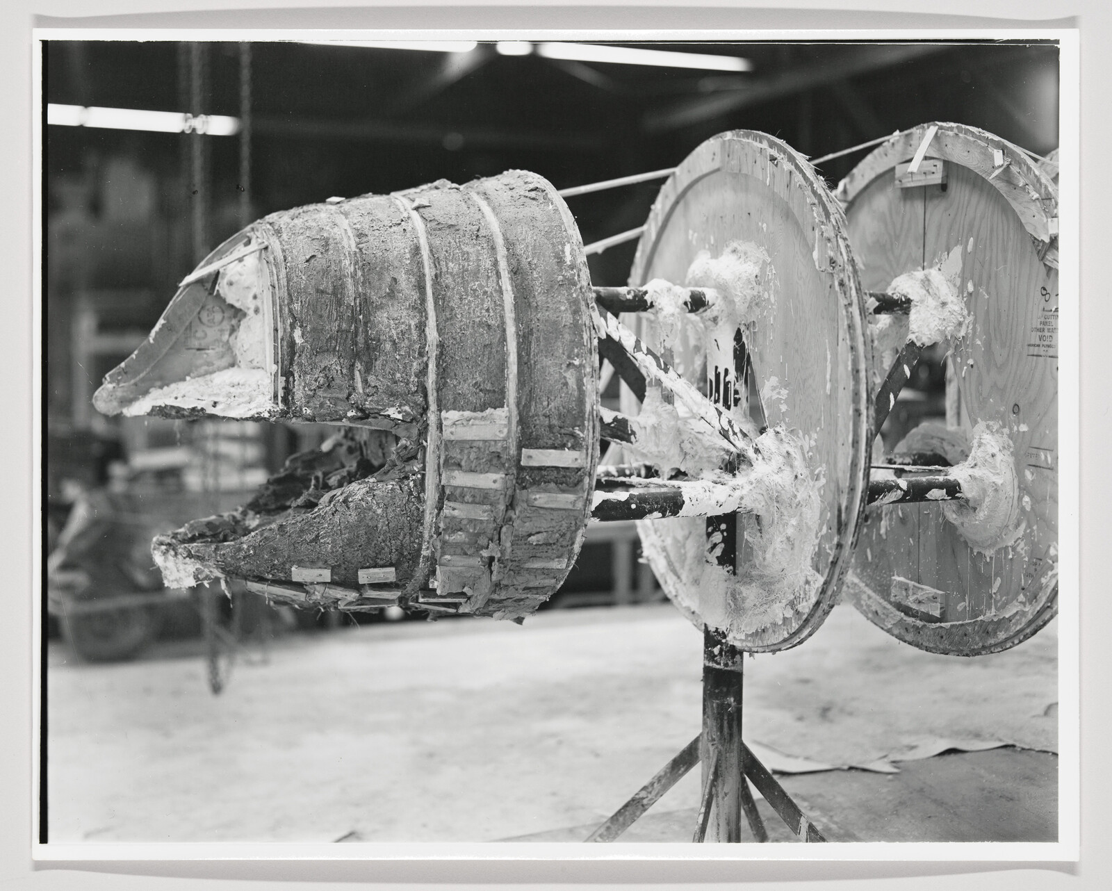 A large plaster puppet head mold mounted on rotating wooden reels in a workshop.
