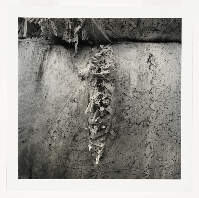 A close-up of tangled perforated paper strips hanging against a textured, scratched surface.