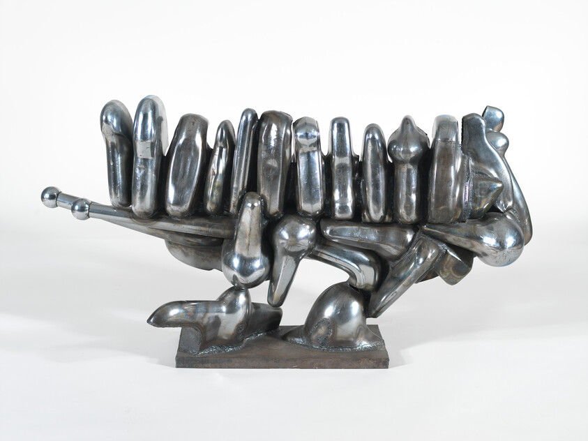 Polished metallic abstract sculpture with rounded, tooth-like vertical forms mounted on a rectangular base.
