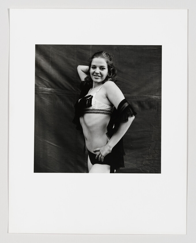 Young woman smiling and posing with one hand behind her head and the other on her hip.