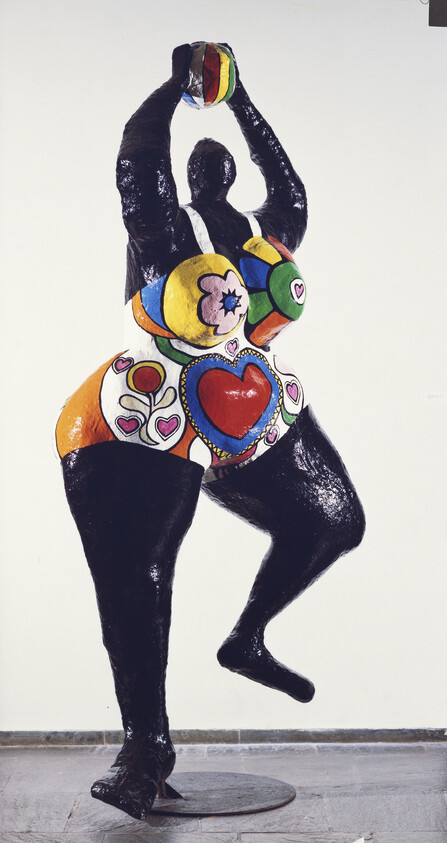 Colorful sculpture of a woman in a swimsuit, balancing on one leg with arms raised, holding a ball.
