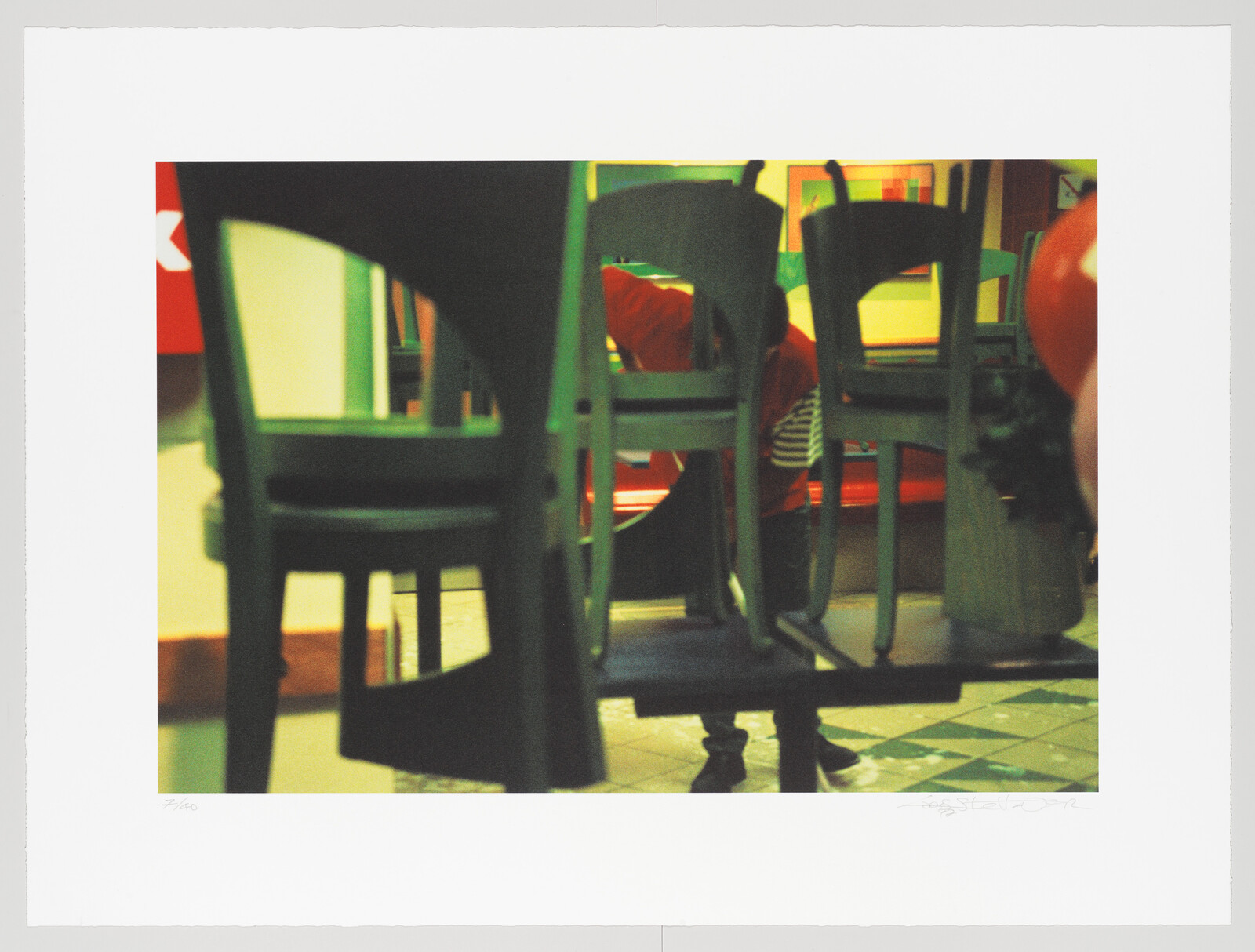 A person in a red shirt stacks chairs on a table in a tiled room.