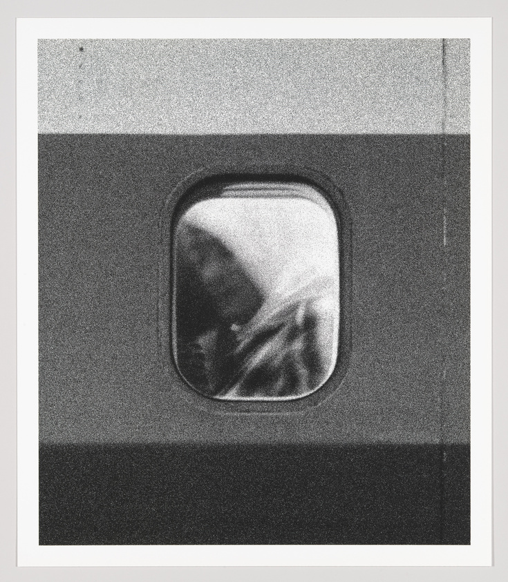 Black and white photo of an airplane window with a blurred view of the wing and sky.