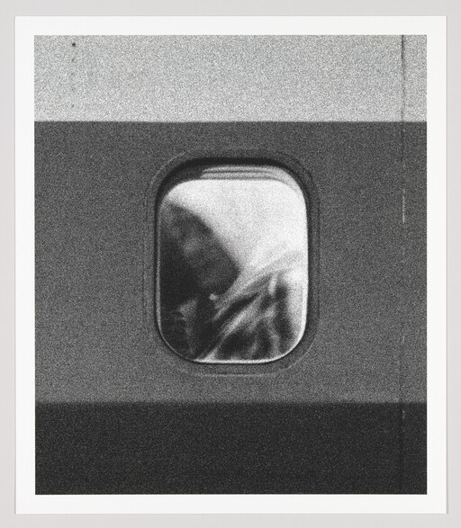 A grainy black-and-white view through an airplane window showing a hooded passenger looking down.