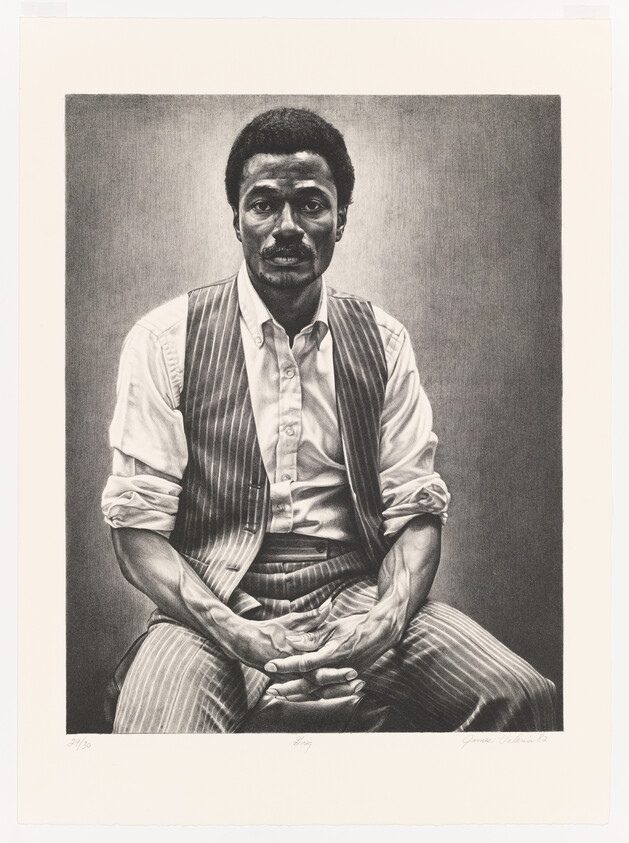 A seated man in a striped vest and rolled-up sleeves sits with hands clasped in his lap.