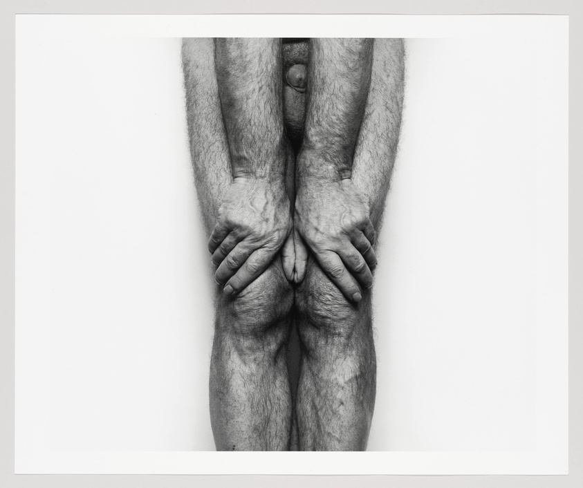 A man's hairy lower body with his hands strongly grasping his kneecaps 