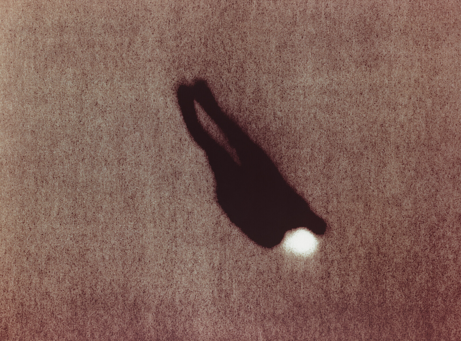 A dark silhouette of a person lying on textured ground with a bright light near the head.