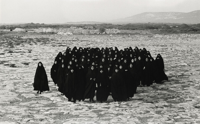 In a large desert, a group of veiled women are standing and staring at the viewer