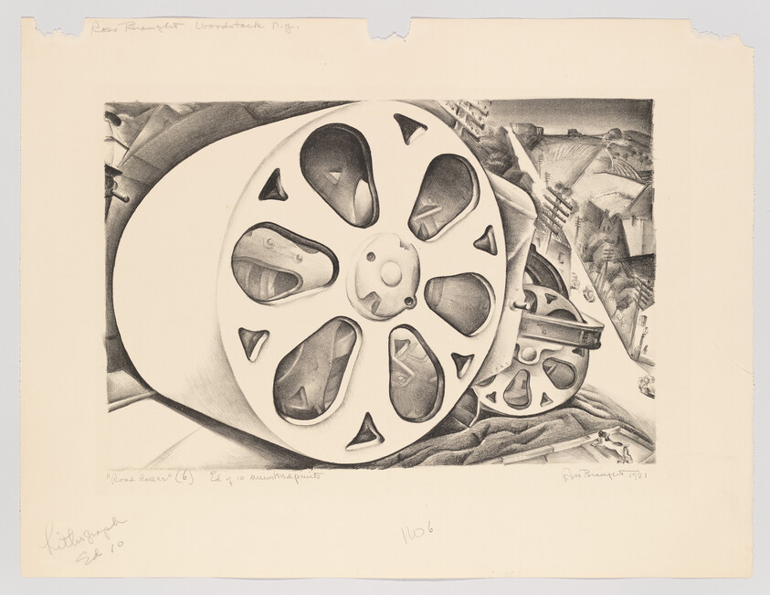 Large metal film reel and smaller gear resting on fabric with industrial landscape in background.
