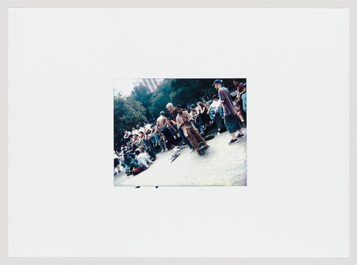 A group of skateboarders and onlookers gather in a park with skateboards on the ground.
