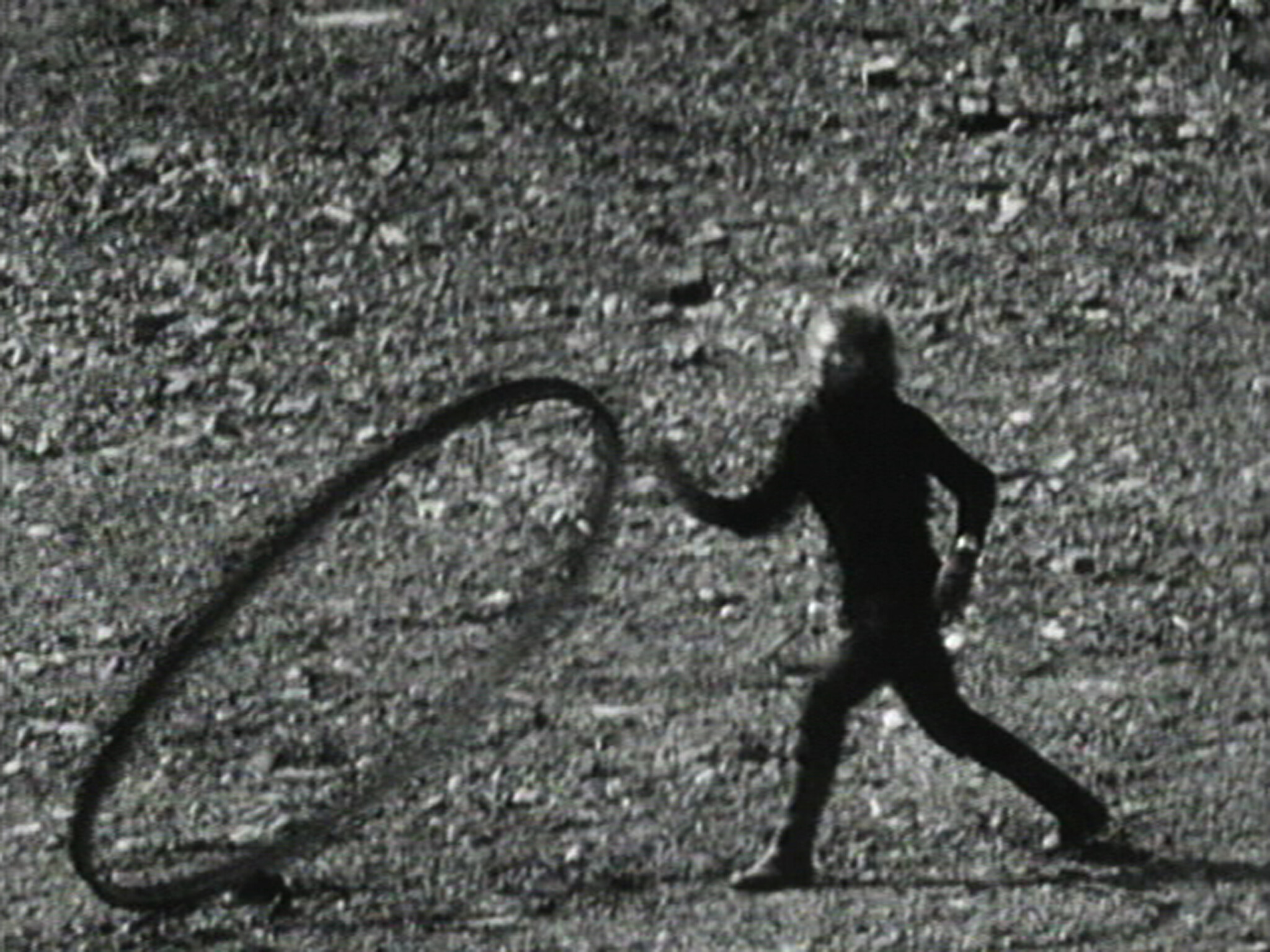 A person in dark clothing runs beside a large rolling hoop on a rough, rocky surface.