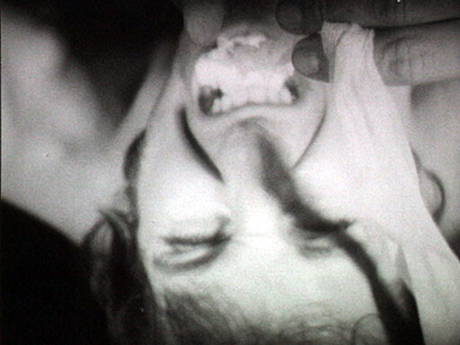 Woman lying upside down with mouth open as a hand touches her face.