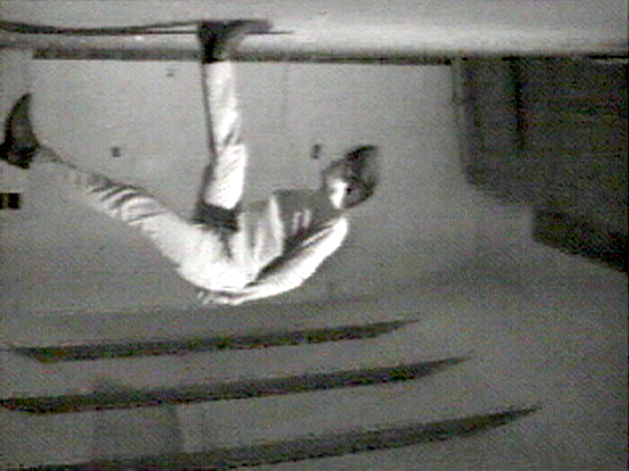 Person hanging upside down from the ceiling, gripping a bar with one hand and one foot.