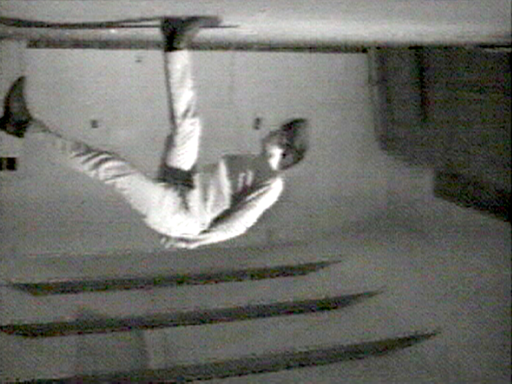 A person upside down with legs spread, appearing to flip or fall in a room.