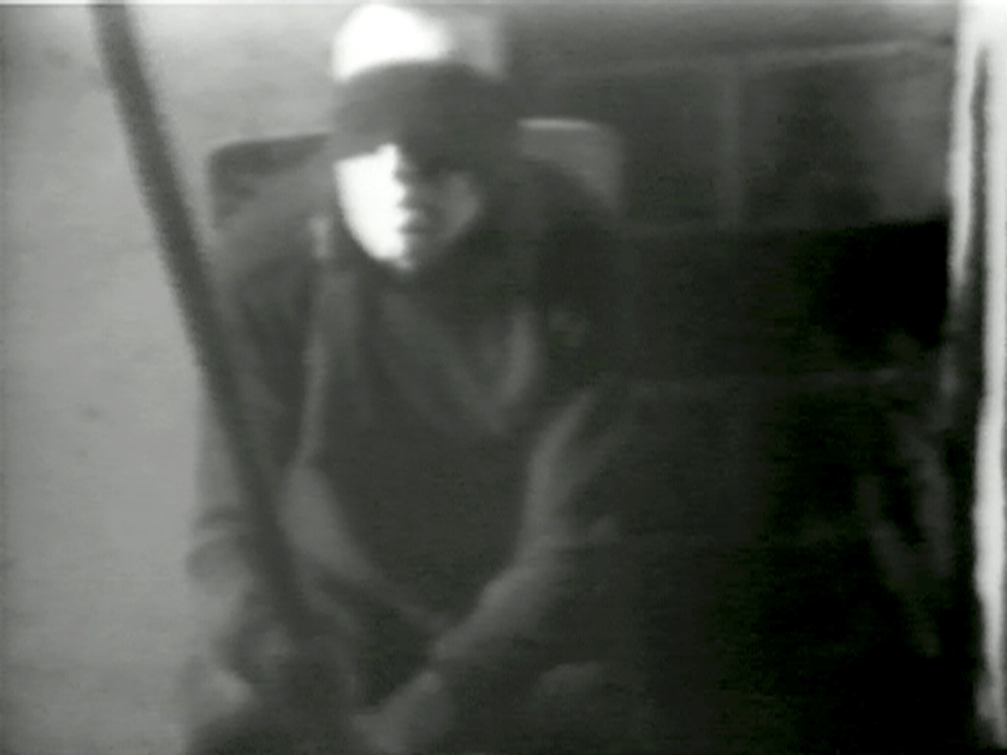 A person with a blindfold sits in a dimly lit room, holding a long object in their hands.