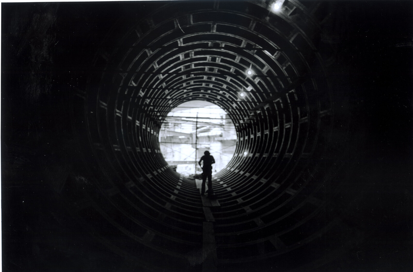 A worker walks toward the light inside a large circular construction tunnel.