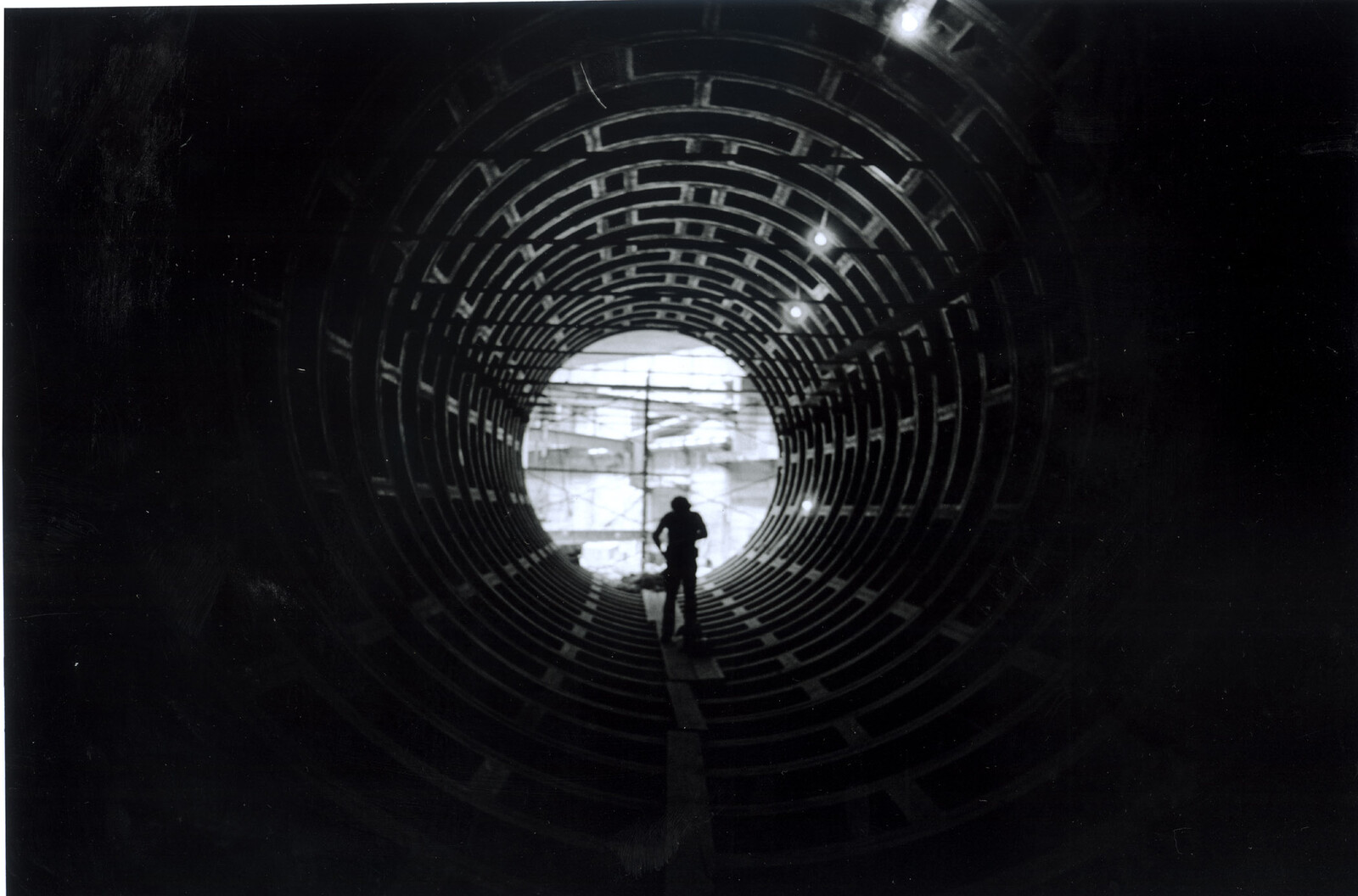A worker walks toward the light inside a large circular construction tunnel.