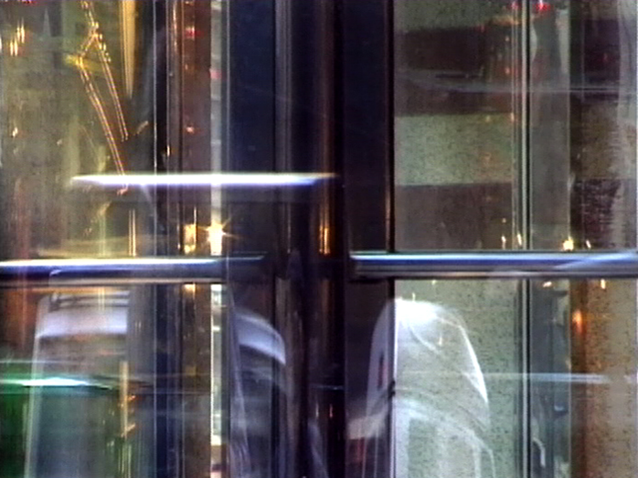 Revolving glass door with metal push bars and blurred reflections of people passing through.