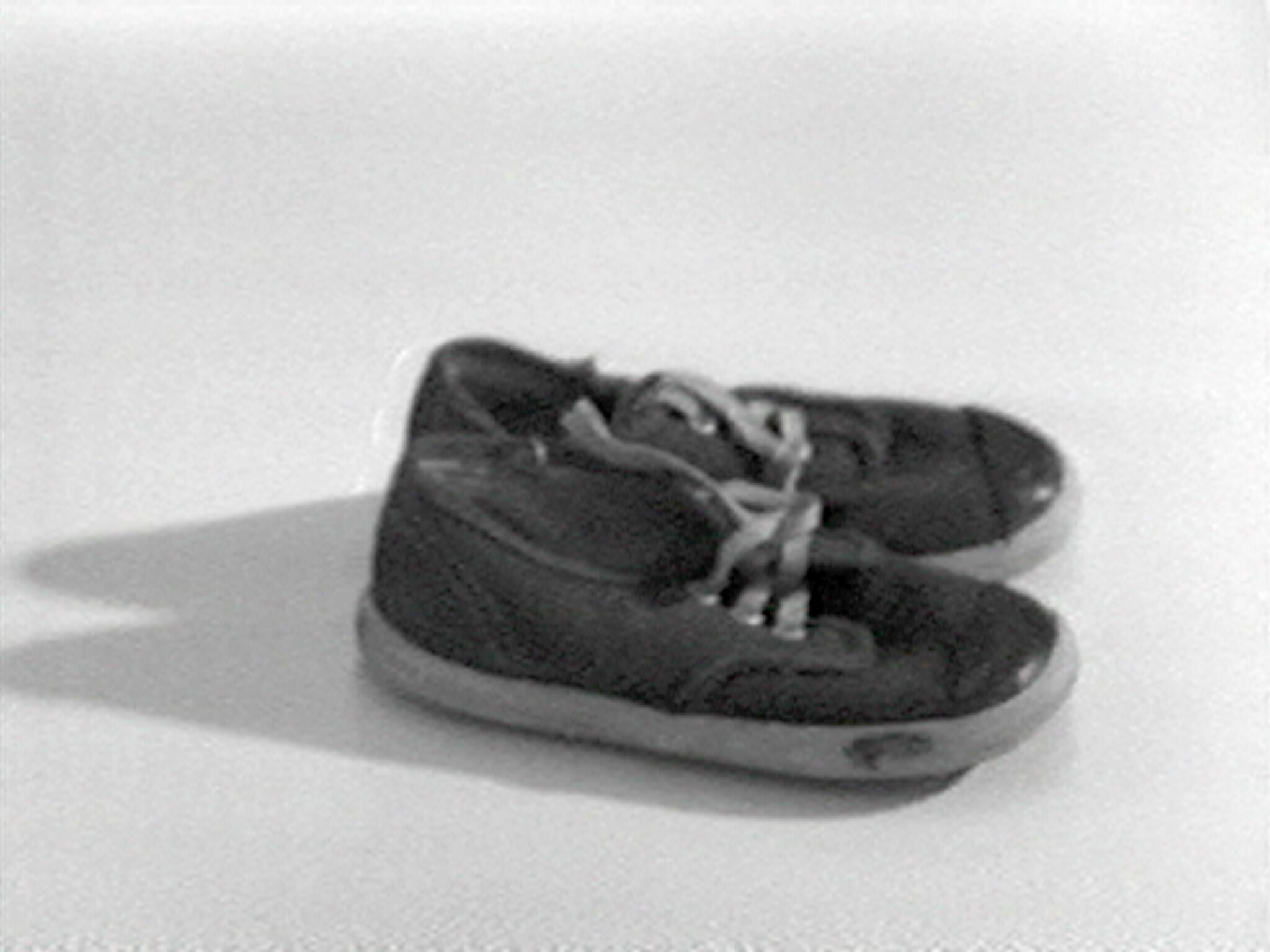 A pair of worn black sneakers with untied laces resting on a plain surface.