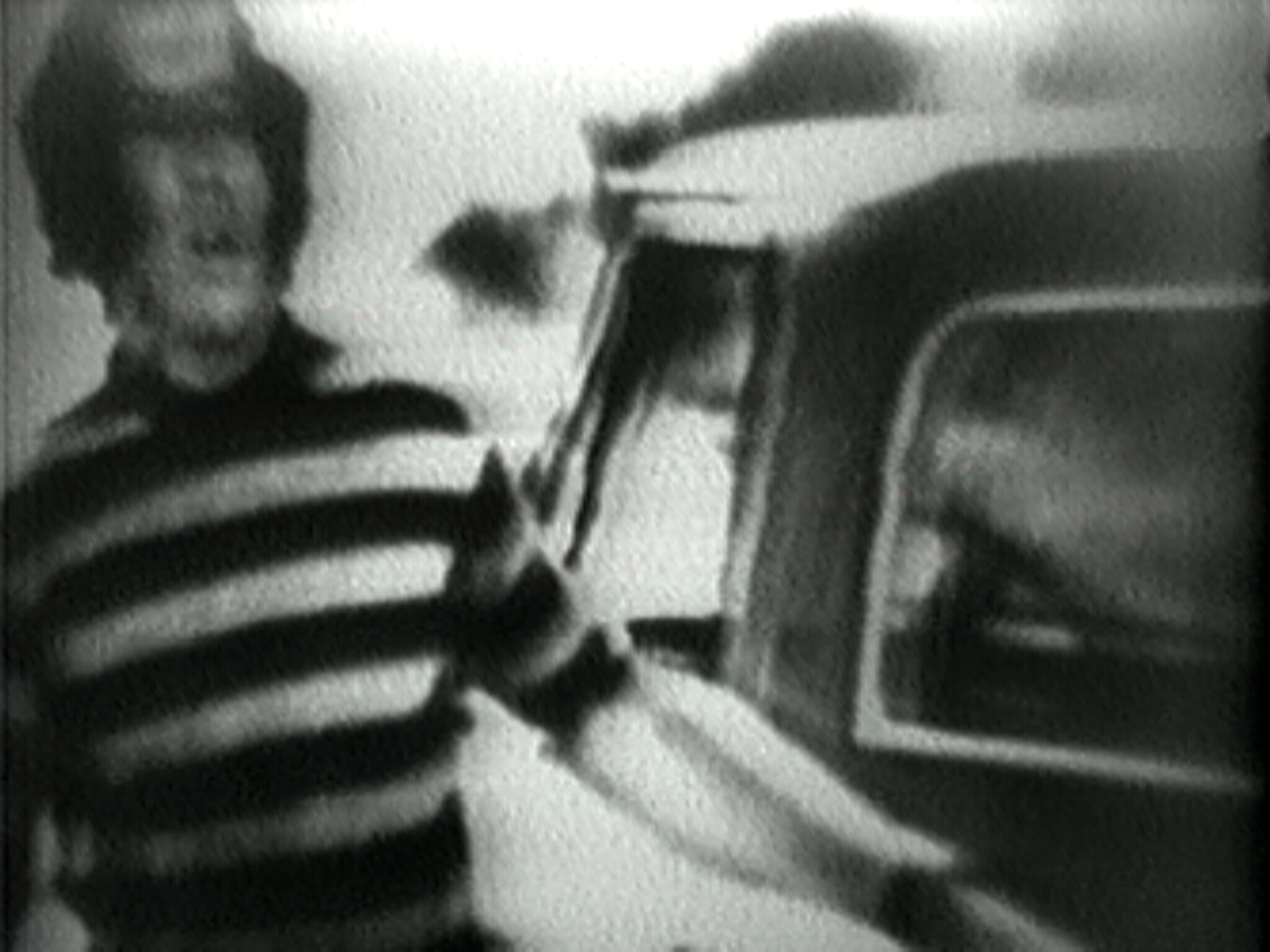 Person wearing a striped shirt stands next to a vehicle, with a blurred and grainy black-and-white effect.