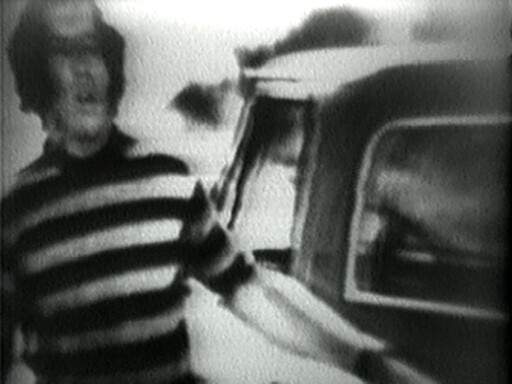 Man in a striped sweater standing beside a car and reaching toward the open car door.