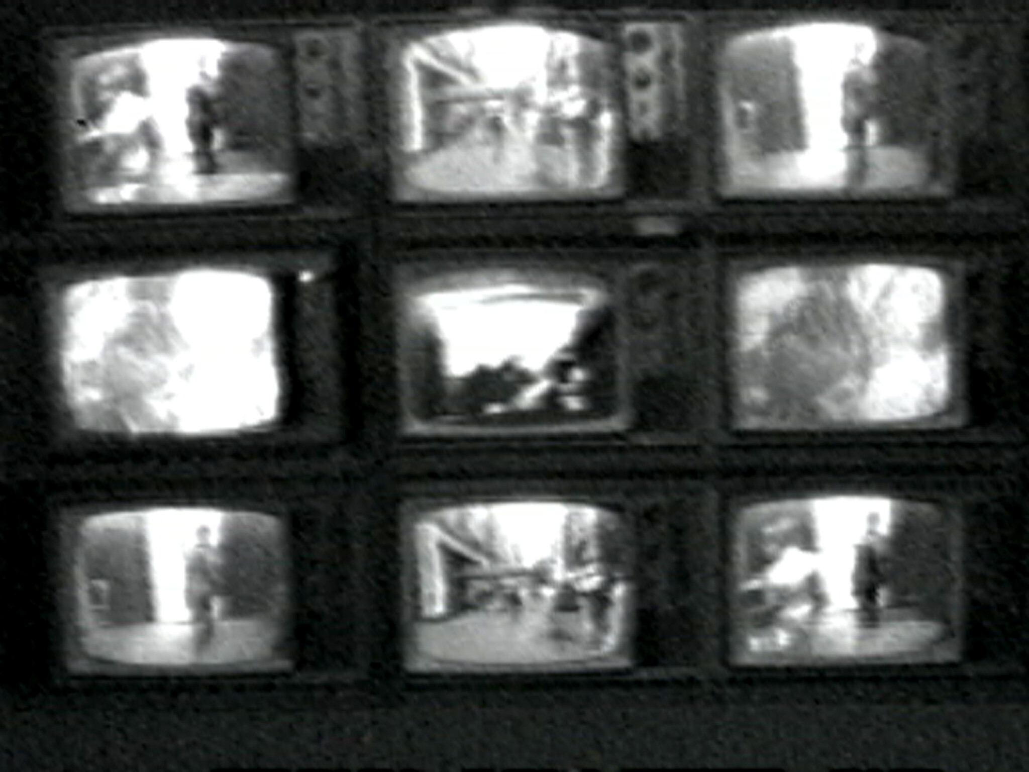 Nine small black-and-white television screens arranged in a three by three grid showing blurry scenes.