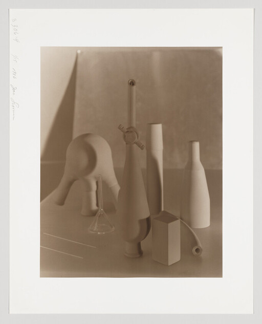 Arrangement of laboratory glassware and geometric shapes on a table in soft light.