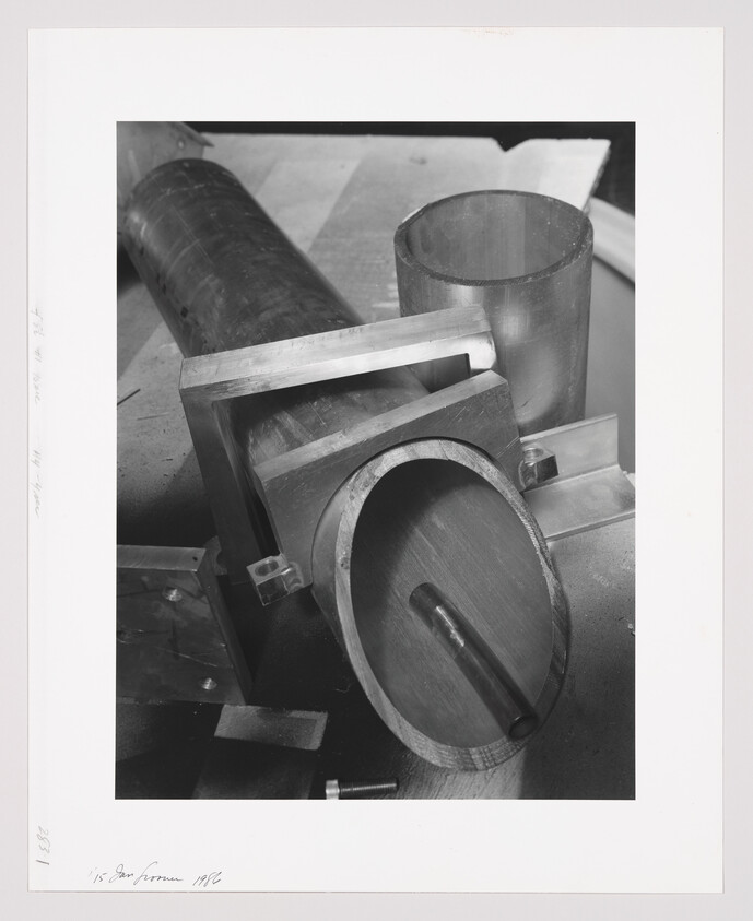 Several metal pipes and round fittings arranged on a workshop bench, one with a small cylindrical rod inside.