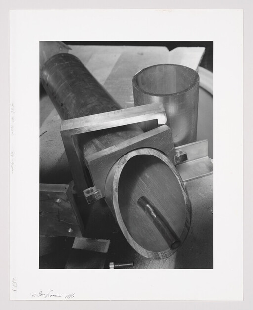 Several metal pipes and round fittings arranged on a workshop bench, one with a small cylindrical rod inside.