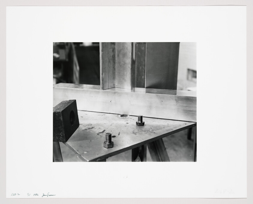 A metal workpiece is clamped to a triangular steel plate with two bolts and nuts.