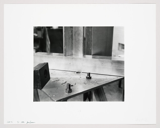 A metal workpiece is clamped to a triangular steel plate with two bolts and nuts.