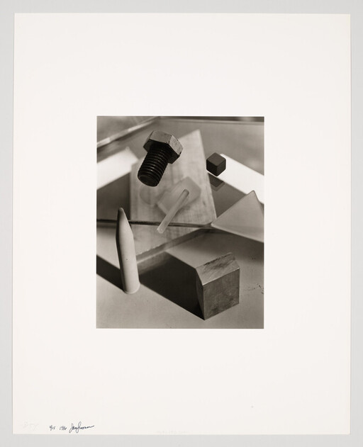 A black bolt, wooden block, and geometric objects arranged on mirrored surfaces casting shadows.