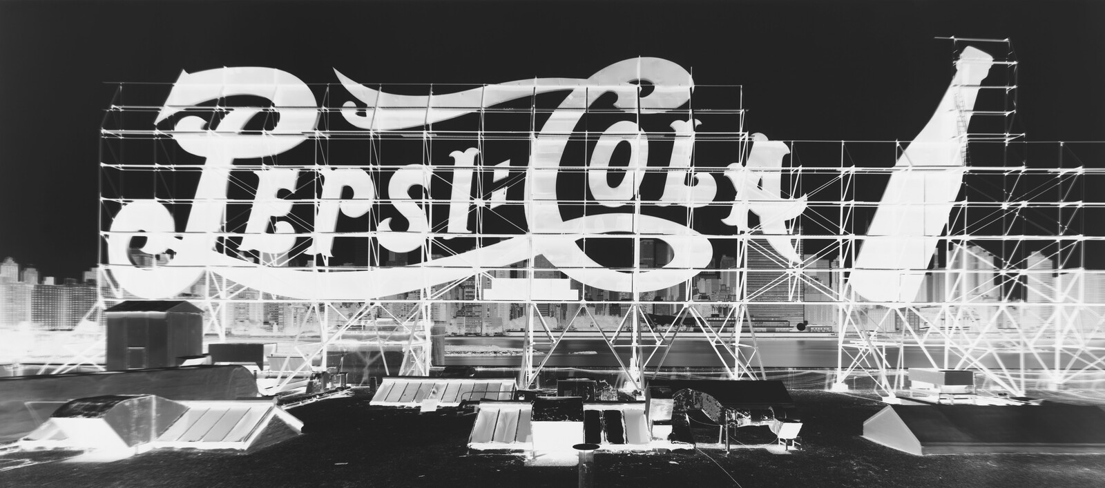 Large illuminated Pepsi-Cola rooftop sign with scaffolding above a city building.