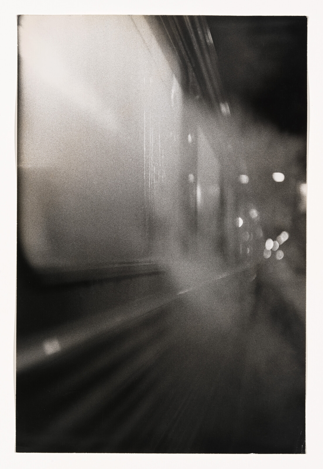 Blurred black-and-white view through a moving train window with streaked lights and reflections.