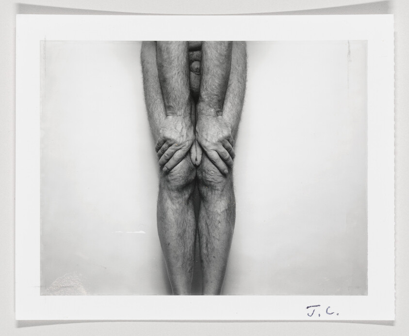 A standing person covering their groin with hands and pressing knees together in a black-and-white photograph.