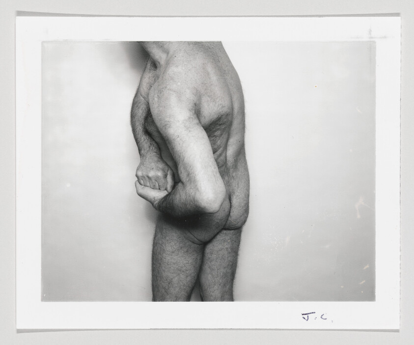 Naked man seen from the side bending his arm behind his back and holding his buttock.