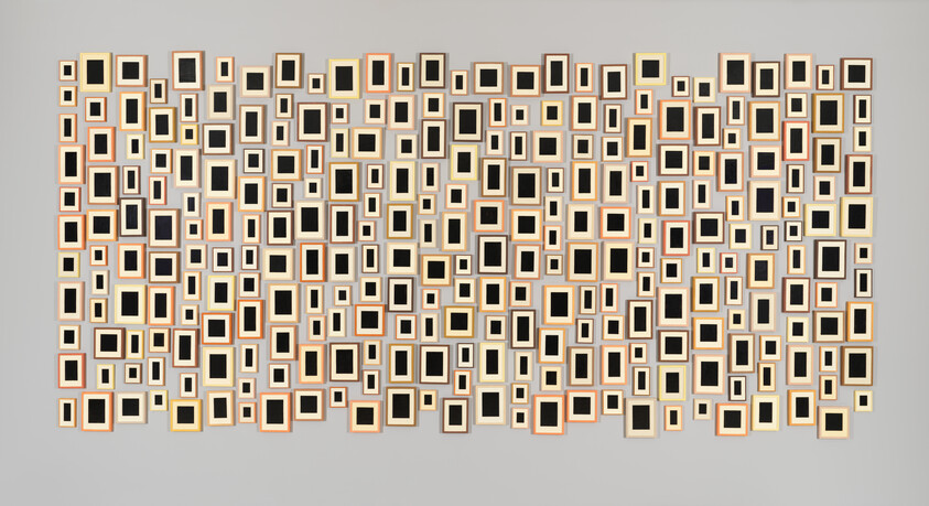 Numerous empty square and rectangular picture frames arranged in irregular grid across a neutral wall.