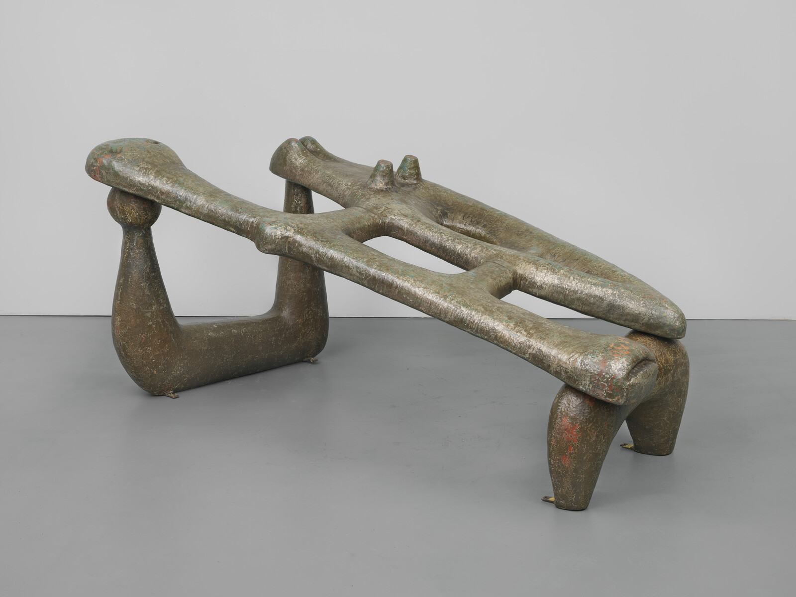 A grey-green punctured organic shape sits askew atop two arches on the floor