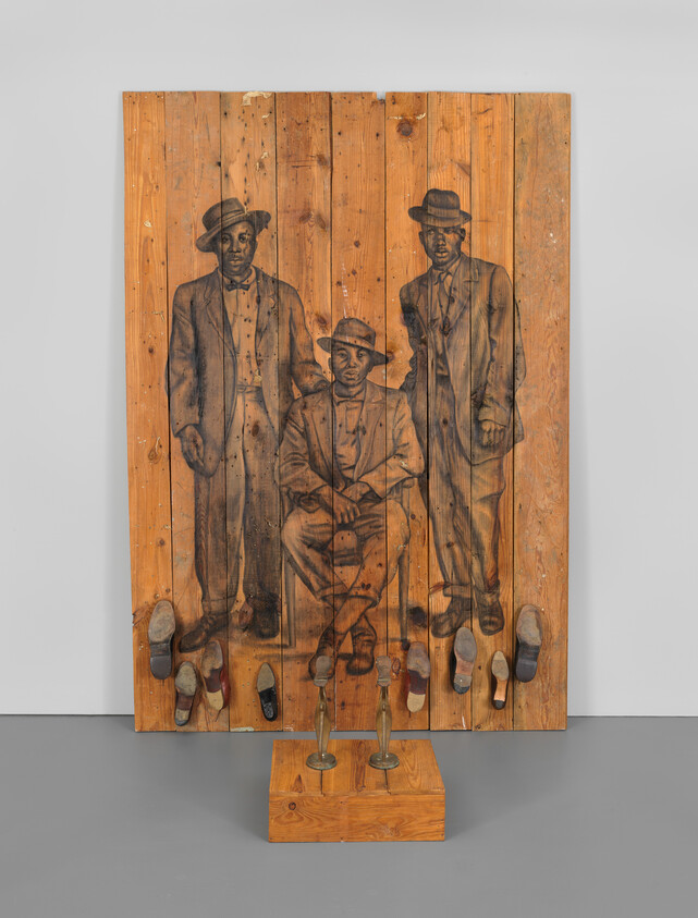 Three men in suits and hats drawn on wooden panels with shoes attached below.